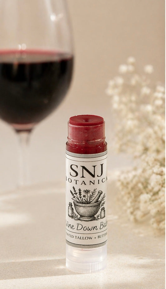 Lip balm with 'SNJ Botanicals' branding next to a glass of red wine.