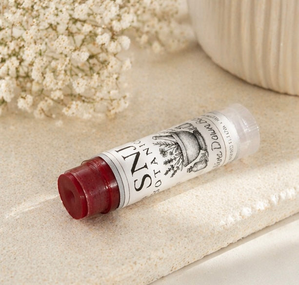 Lip balm tube with white label on a textured surface with flowers in the background