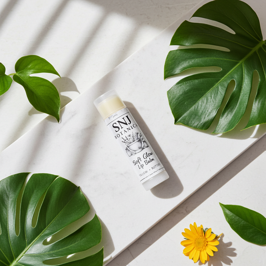 Lip balm with 'SNJ' branding on a light surface with green leaves and a yellow flower.