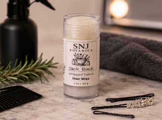 Hair wax stick with branding on a marble surface with hair accessories and a plant.